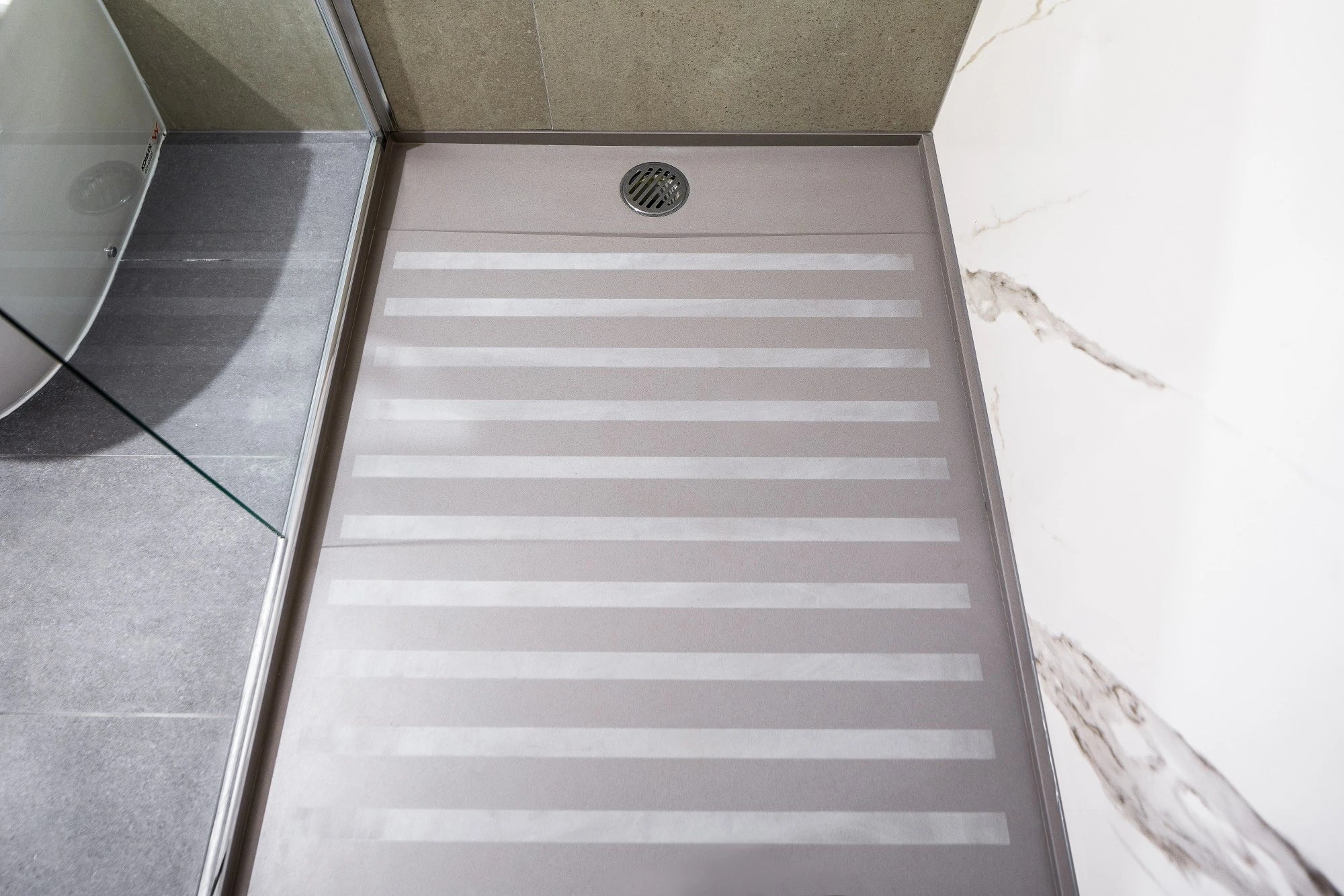 Silestone Kensho shower base with light gray striped anti-slip surface and center drain — engineered quartz countertops fabricated and installed by Signature...