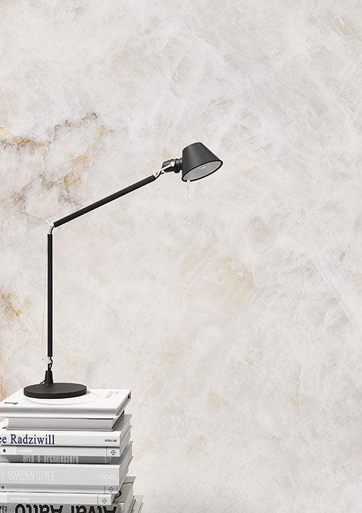 Black adjustable desk lamp on stacked books against textured wall — modern lighting for spaces with custom countertops fabricated and installed by Signature ...