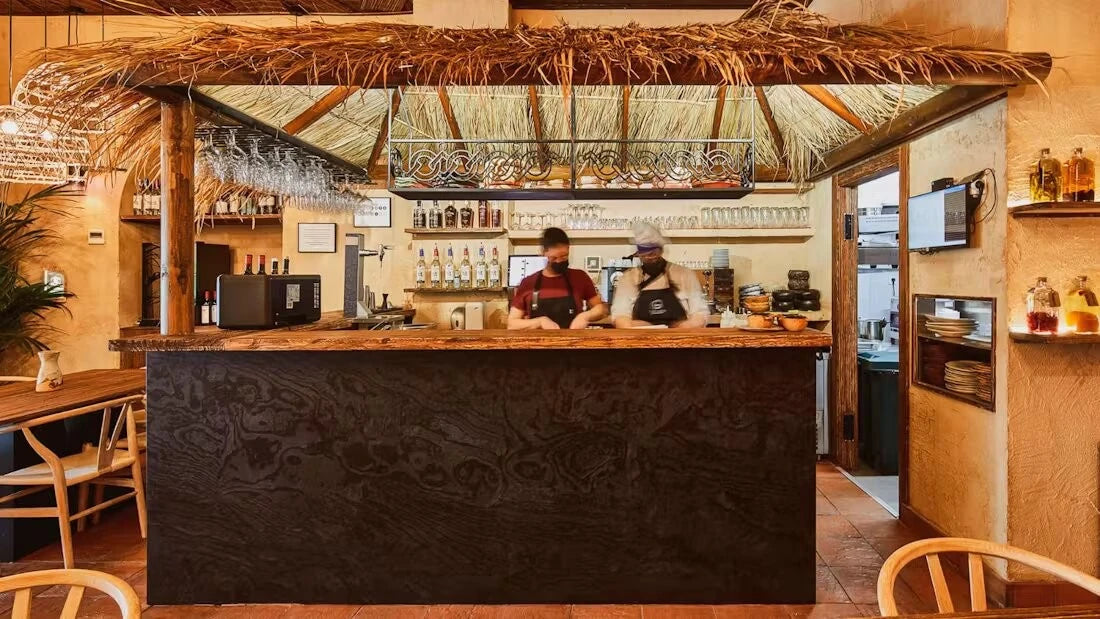 Dekton Liquid Embers bar countertop with dark textured finish and live edge wood support under thatched canopy — premium dekton surfaces fabricated and insta...