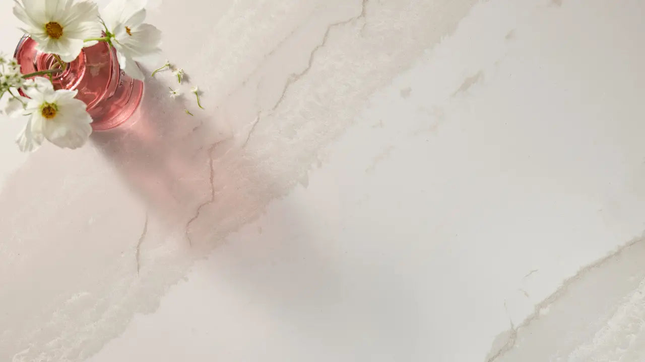 Quartz countertop surface with white marble veining and pink glass vase with white flowers — expert countertop fabrication by Signature Stone Las Vegas