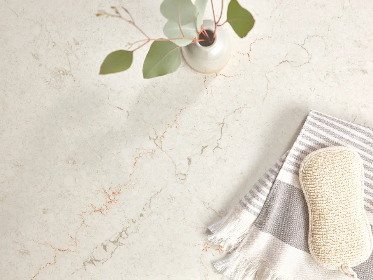 Marble surface with white background and gray veining alongside striped towel and natural elements — custom countertops fabricated and installed by Signature...