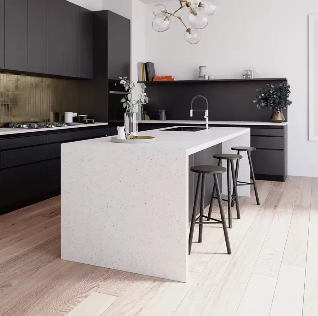 Modern kitchen interior featuring a large white quartz countertop island with black bar stools, matte black cabinetry, wooden flooring, and minimalist decor accents.