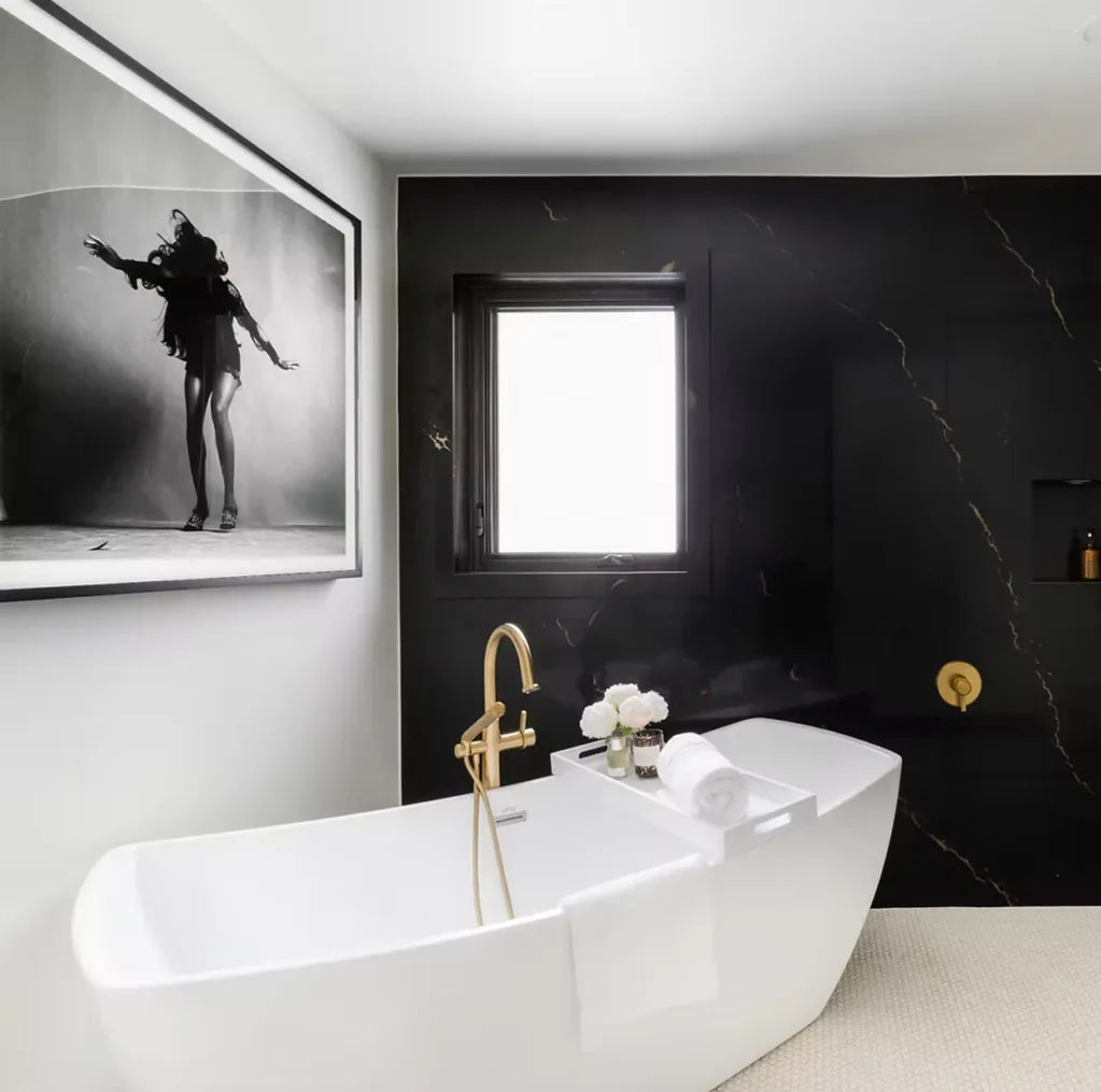 Modern bathroom with white freestanding tub, gold faucet, and black quartz wall with veining.