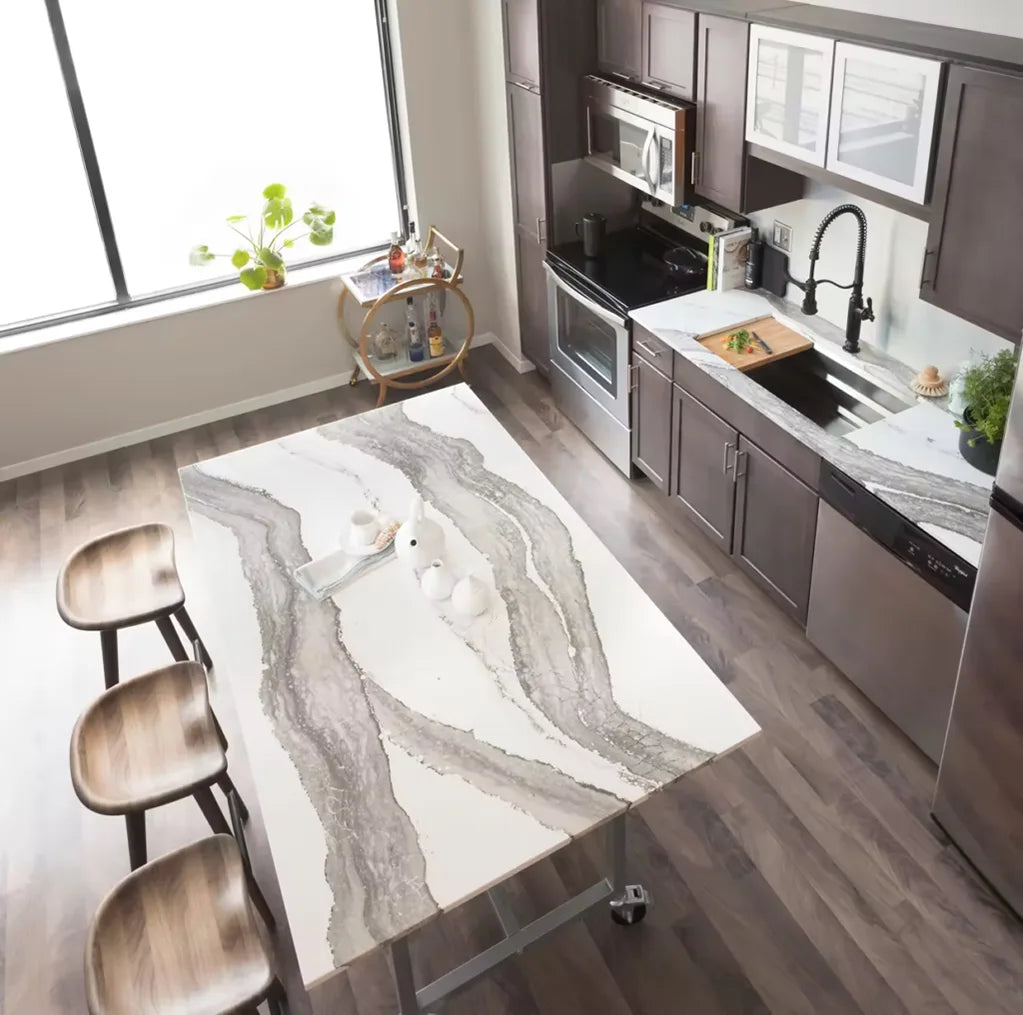 Modern kitchen featuring dark wood cabinets, stainless steel appliances, and a large quartz countertop island with flowing gray and white veining, paired with wooden bar stools.