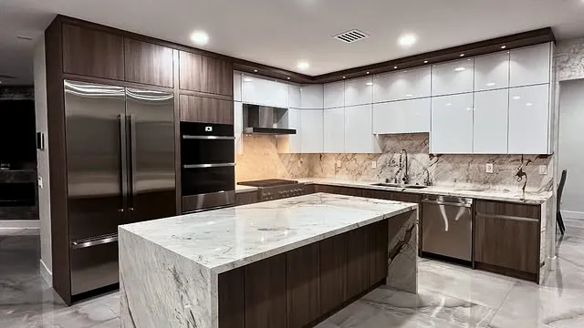 Modern kitchen with glossy white upper cabinets, dark wood lower cabinets, stainless steel appliances, and a large marble island. Marble backsplash and floors, under-cabinet lighting, and sleek kitchen countertops complete the contemporary design.